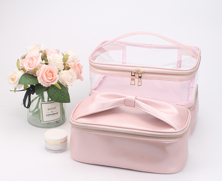 Two-layer pink satin cosmetic bag with transparent PVC upper compartment, bow decoration, top hand strap and metal double zippers