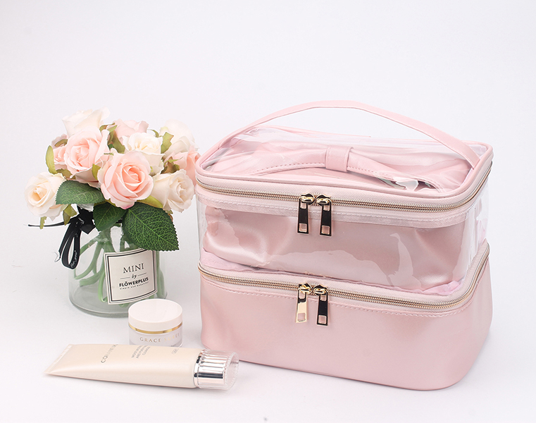 Two-tier pink satin cosmetic bag with transparent PVC upper layer, bow decoration, top hand handle and double gold metal zippers